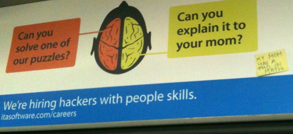 A public transit ad shows a brain with two hemispheres. A box pointing to the left hemisphere asks, 'Can you solve one of our puzzles?' A box pointing to the right hemisphere asks, 'Can you explain it to your mom?' Text at the bottom says, 'We're hiring hackers with people skills. itasoftware.com/careers' There is a real yellow sticky note stuck on to the ad that says, 'My mom has a PhD in math.'